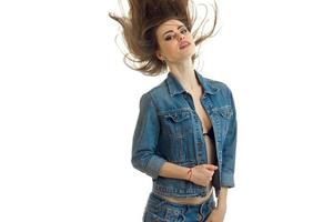 Schönes junges Mädchen in Jeansjacke posiert für die Kamera und ihr Haar fliegt durch die Luft foto