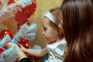 Mutter schmückt den Weihnachtsbaum mit ihrem kleinen Mädchen foto