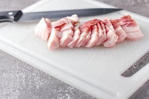 durchwachsenes schweinefleisch wird auf einem weißen schneidebrett in der küche geschnitten. nahaufnahme schnittfolie schweinebauch roh foto