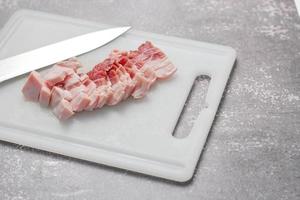 durchwachsenes schweinefleisch wird auf einem weißen schneidebrett in der küche geschnitten. nahaufnahme schnittfolie schweinebauch roh foto