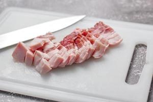 durchwachsenes schweinefleisch wird auf einem weißen schneidebrett in der küche geschnitten. nahaufnahme schnittfolie schweinebauch roh foto