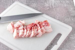 durchwachsenes schweinefleisch wird auf einem weißen schneidebrett in der küche geschnitten. nahaufnahme schnittfolie schweinebauch roh foto