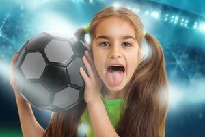 lustiges Mädchen mit einem Fußball zeigt Tonque foto