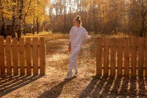 Mädchen steht im Herbst in der Nähe eines Holzzauns foto