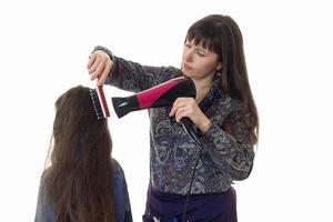 Erwachsene Stylistin macht einem kleinen Mädchen mit langen Haaren eine Frisur foto