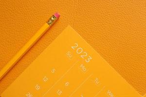 orange Farbe 2023 Jahreskalender und ein Bleistift auf dem Tisch foto