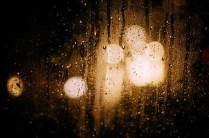 auf dem glas spiegeln sich runde spiegelungen des verschwommenen lichts von autoscheinwerfern während des regens. foto