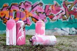 Ein paar gebrauchte Farbdosen liegen auf dem Boden in der Nähe der Wand mit einem schönen Graffiti-Gemälde in rosa und grünen Farben. Street-Art-Konzept foto