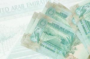 10 VAE-Dirham-Scheine liegen im Stapel auf dem Hintergrund einer großen halbtransparenten Banknote. abstrakte Darstellung der Landeswährung foto