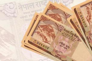 10 nepalesische Rupien-Scheine liegen im Stapel auf dem Hintergrund einer großen halbtransparenten Banknote. abstrakte Darstellung der Landeswährung foto
