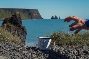 Schließen Sie herauf die männliche Hand, die zum Becher auf Felsenkonzeptfoto greift foto