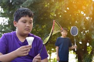 junger asiatischer junge hält traurig gebrochenen rahmen-badmintonschläger in der hand, während er mit seinem freund außerhalb des hauses badminton spielt, badminton-konzept im freien, weicher und selektiver fokus. foto