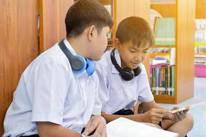 soft fucus von zwei asiatischen jungen studenten hören medien, lesen und beraten sich über lieblingsbücher in der schulbibliothek foto