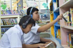 soft fucus von zwei asiatischen jungen studenten hören medien, lesen und beraten sich über lieblingsbücher in der schulbibliothek foto