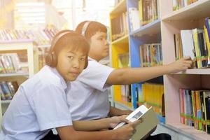 soft fucus von zwei asiatischen jungen studenten hören medien, lesen und beraten sich über lieblingsbücher in der schulbibliothek foto