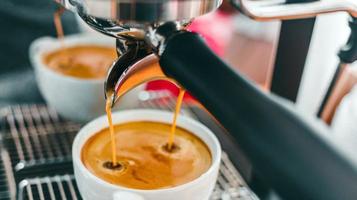 Nahaufnahme der Kaffeeextraktion aus der Kaffeemaschine mit einem Siebträger, der Kaffee in eine Tasse gießt, Espresso aus der Kaffeemaschine im Café foto