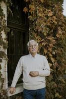 älterer Mann, der am Herbsttag am Fenster steht foto