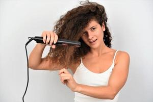 Mädchen mit welligem Haar bügelt, glättet unordentliche Locken, Keratin-Therapiebehandlung foto