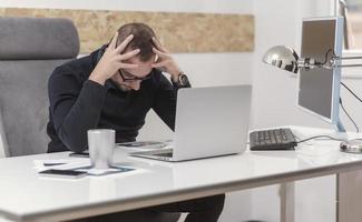 Junger Geschäftsmann, der zu Hause mit Laptop und Papieren auf dem Schreibtisch arbeitet foto