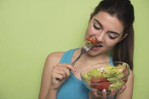 Porträt eines glücklichen, verspielten Mädchens, das frischen Salat aus einem Bogen isst foto