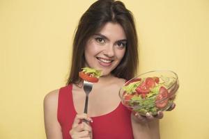 Porträt eines glücklichen, verspielten Mädchens, das frischen Salat aus einem Bogen isst foto