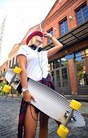 Schönes Hipster-Mädchen mit Skateboard und Sonnenbrille in der Stadt. foto