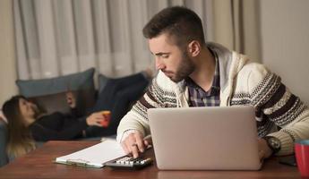 junge paare, die finanzen verwalten und ihre bankkonten mit einem laptop überprüfen. frau und mann erledigen zusammen papierkram und zahlen online steuern auf notebook-pc foto