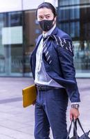 gut aussehender asiatischer geschäftsmann, der covid-maske und anzug trägt, im freien spazieren geht, erfolgreicher manager während der pause in der stadt spazieren geht. foto