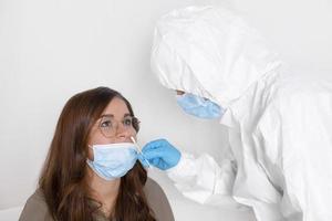 Covid-19-Test. laborangestellter mit persönlicher schutzausrüstung, der junge frau mit nasenabstrichmethode auf coronavirus testet. foto