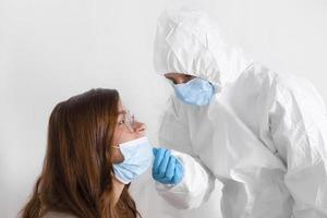 Covid-19-Test. laborangestellter mit persönlicher schutzausrüstung, der junge frau mit nasenabstrichmethode auf coronavirus testet. foto