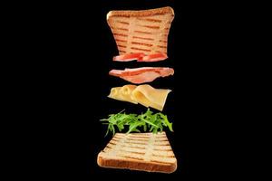 Frisches Sandwich mit fliegenden Zutaten auf schwarzem Hintergrund isoliert foto