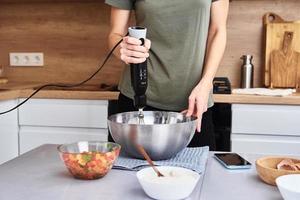 Frau in der Küche, die einen Kuchen kocht. hände schlagen den teig mit einem elektrischen mixer foto