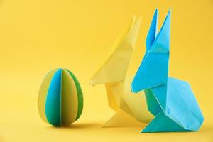 zwei Origami-Esater-Kaninchen aus Papier und farbiges Ei auf gelbem Hintergrund foto