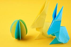 zwei Origami-Esater-Kaninchen aus Papier und farbiges Ei auf gelbem Hintergrund foto