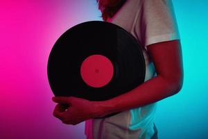 Frau hält Retro-Vinyl-Disc mit Neonlicht foto