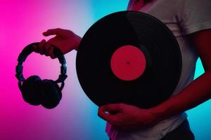 frau hält retro-vinylscheibe und kopfhörer mit neonlicht foto