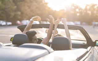 freunde, die spaß bei der autoreise um die welt haben. Verliebtes Paar mit erhobenen Armen auf einem Cabrio. foto