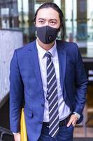 gutaussehender asiatischer geschäftsmann mit covid-maske und anzug, der im freien geht foto