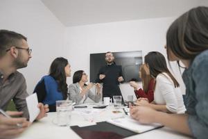 Executive Leader im Gespräch mit einer glücklichen, vielfältigen Mitarbeitergruppe bei einer Unternehmensbürobesprechung, foto