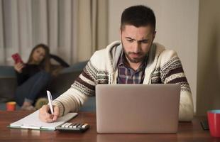 junge paare, die finanzen verwalten und ihre bankkonten mit einem laptop überprüfen. frau und mann erledigen zusammen papierkram und zahlen online steuern auf notebook-pc foto