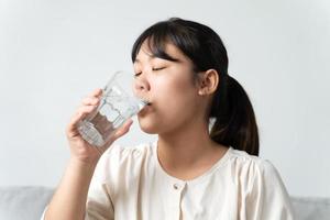 Gesunde, schöne junge Frau, die ein Glas Wasser hält und auf der Couch im Wohnzimmer sitzt. foto