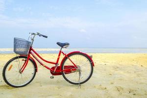 Rotes Fahrrad, das sich an einem sonnigen Tag am Strand lehnt foto