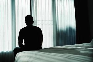 Silhouette depressiver Mann sitzt traurig auf dem Bett im Schlafzimmer. Trauriger asiatischer Mann, der an Depressionen, Schlaflosigkeit leidet, wacht auf und sitzt allein auf dem Bett im Schlafzimmer. Depression Gesundheit Menschen Konzept. foto