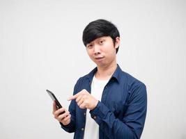 Junger Mann zeigt mit dem Finger auf das Handy in seiner Hand und fühlt sich verwirrt auf weißem Hintergrund foto