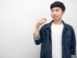 asiatischer mann jeanshemd hält bitcoin und schaut auf kopienraum foto