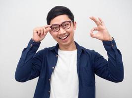 fröhlicher mann mit brille berührt seine brille und macht hand ok porträt weißen hintergrund foto