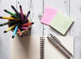 Stift buntes Array Rundschreiben im Karton mit offenem Notizbuch leer mit zwei silbernen Stiften auf weißem Holztisch mit Briefpapier und Naturlicht der Draufsicht des Sonnenideenkonzepts, Wirtschaft und Bildung foto