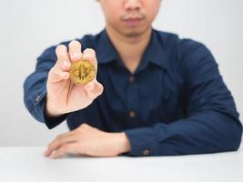 Mann sitzt am Schreibtisch und zeigt Gold-Bitcoin in seiner Hand foto