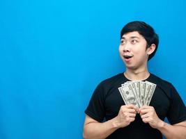 asiatischer mann, der geld hält, fühlt sich aufgeregt und schaut auf den blauen hintergrund des kopierraums foto