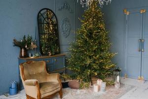 Weihnachten und Neujahr schmücken das dunkle Interieur des Raumes. ein festlich geschmücktes Zimmer mit Kamin, Sessel und Spiegel. festliche weihnachtsnacht mit lichtern foto